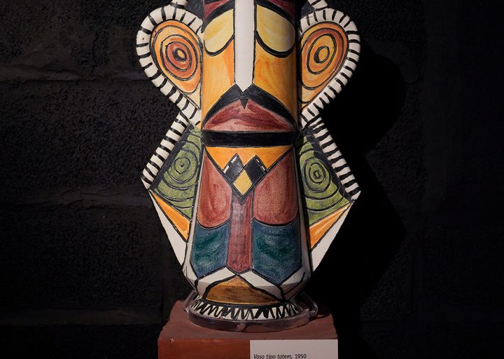 Ceramica smaltata di Brajo Fuso dai colori vivaci posta su un piedistallo. Ripropone una figura umana, con dei baffi dipinti sul viso. I motivi geometrici lungo il busto ricalcano un completo giacca e cravatta.
